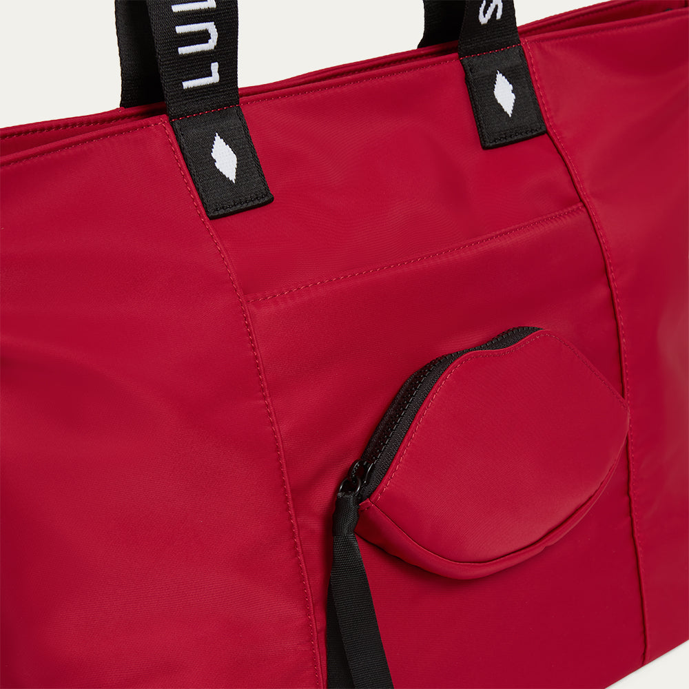 Red tote bag with black handles and a lip-shaped pocket on a white background