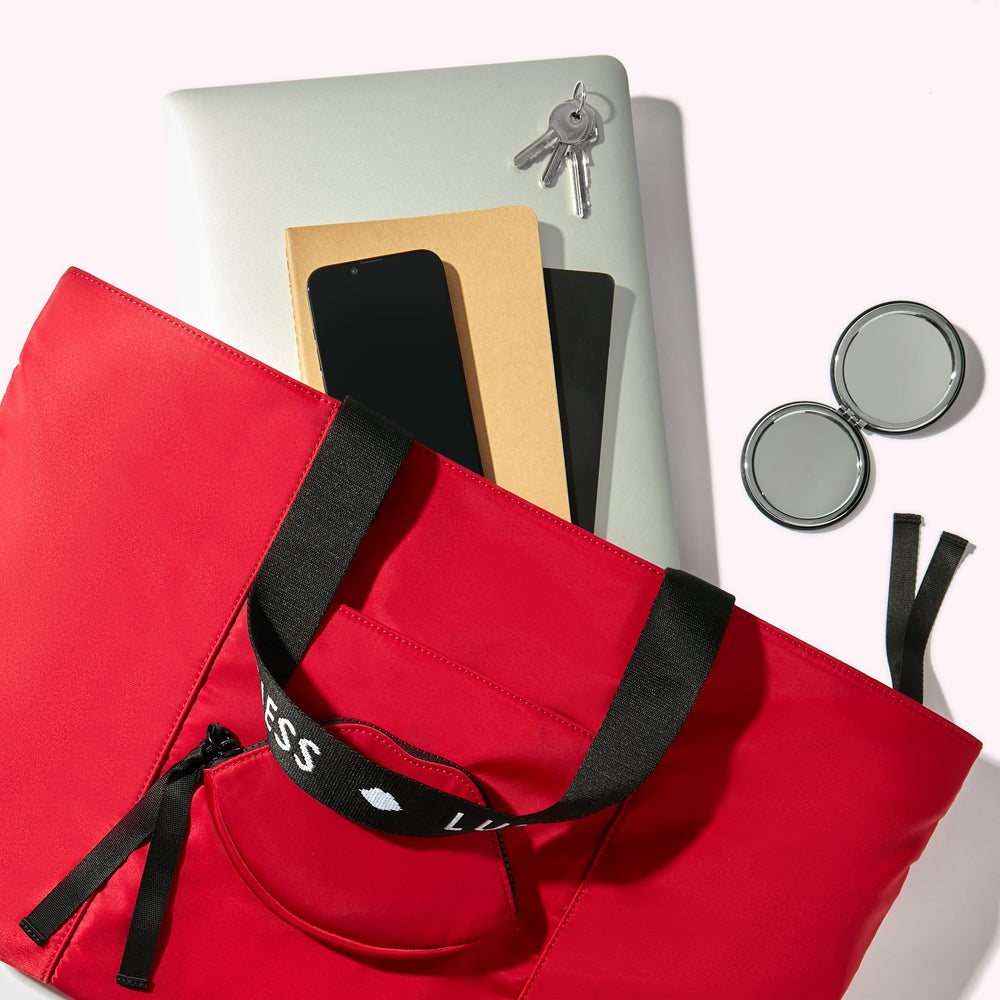 A red nylon tote bag handbag with a laptop, notebooks, smartphone, keys and compact mirror spilling out.