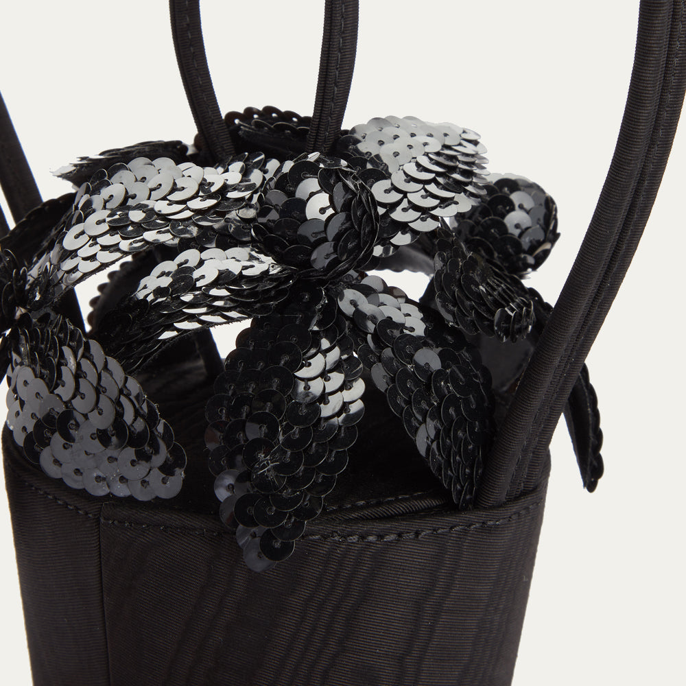 Detail close up image of sequin flowers on top of a black satin moire bag.
