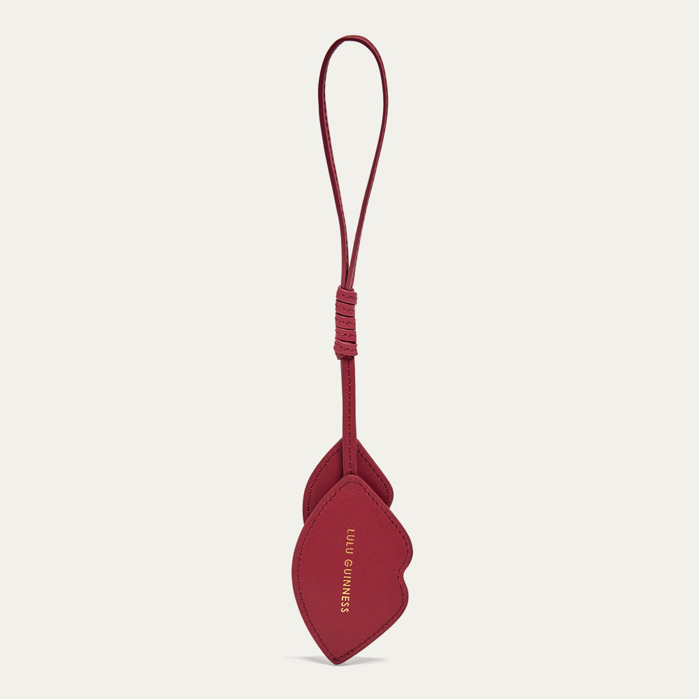 Back images of a red leather lip shaped charm with a foil printed 'Lulu Guinness' logo on a light gray background