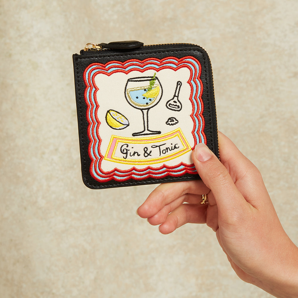 Hand holding a small wallet with 'Gin & Tonic' design on a beige background