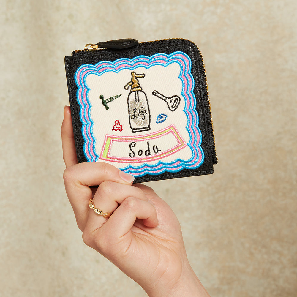 Hand holding a small black wallet with colorful design on a beige background