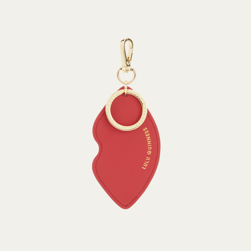 Red lip-shaped keychain with gold ring on a light beige background