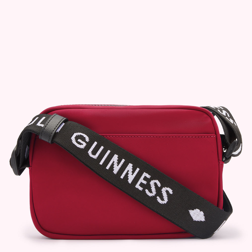 Red crossbody bag with black strap that says "Lulu Guinness" in white lettering.
