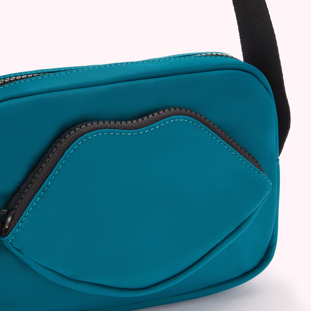 Close-up of a teal crossbody bag with a lip-shaped zipper pocket.
