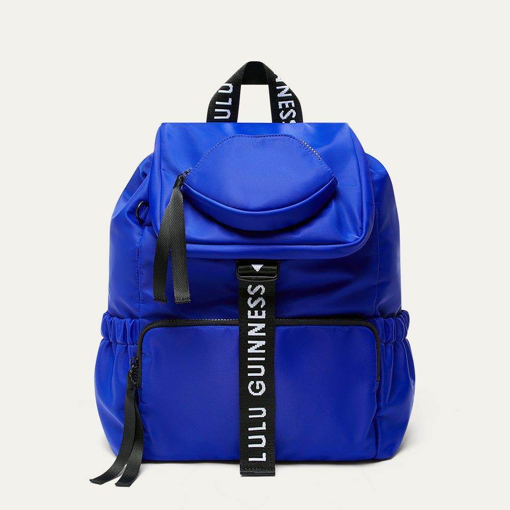 Cobalt blue backpack with black branded 'Lulu Guinness' straps and a lip shaped pocket on a white background