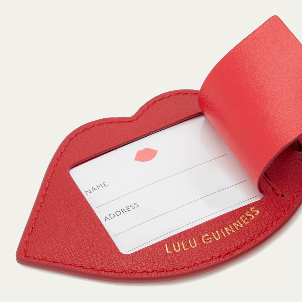 Red lip-shaped luggage tag with a white label inside, featuring 'Lulu Guinness' branding.