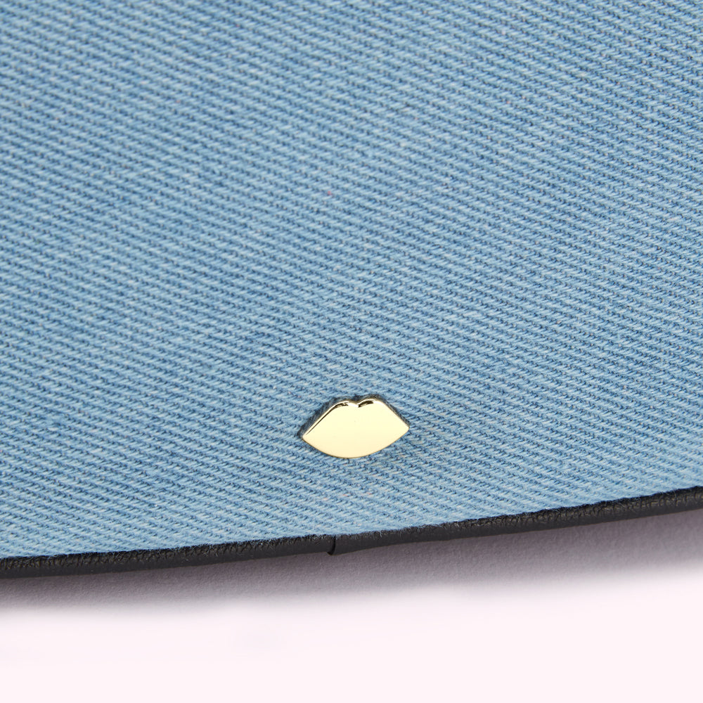 Close-up of a light blue denim fabric with a gold lip-shaped emblem.
