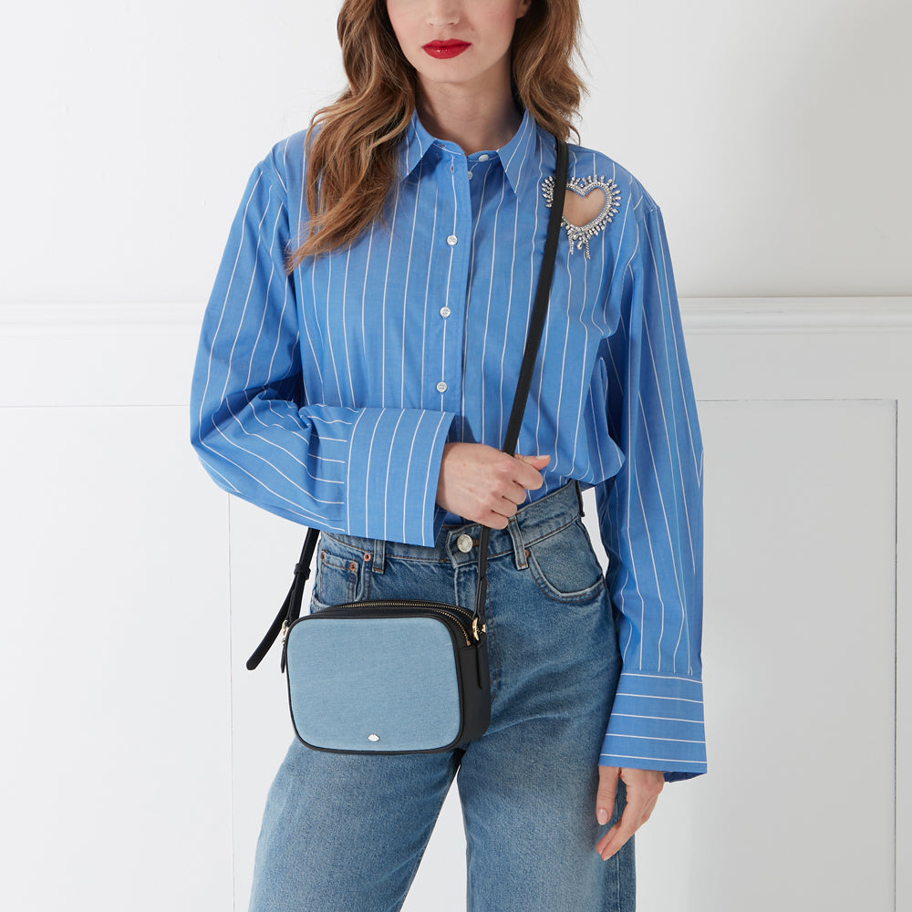 A woman in a blue striped shirt and jeans is wearing a light blue and black crossbody bag.
