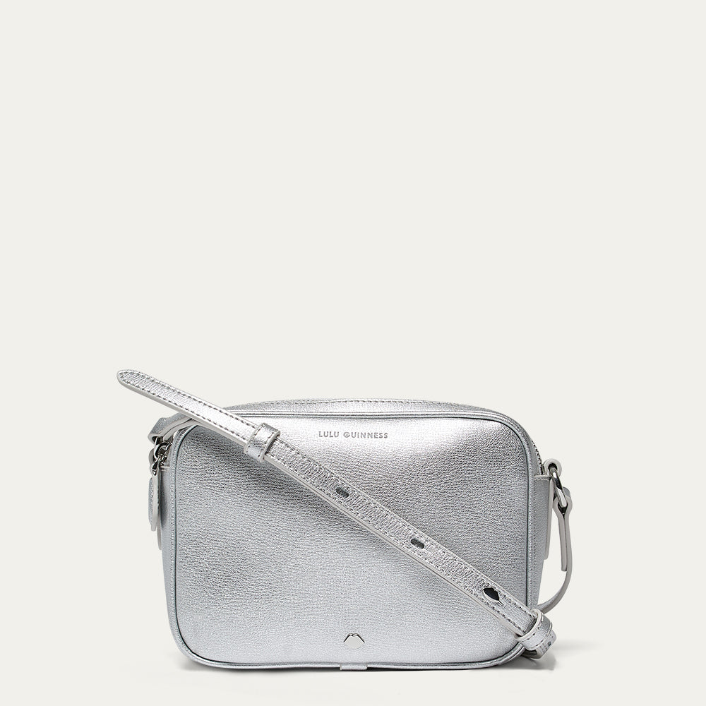 Silver crossbody bag with a lip shaped silver stud on a light gray background