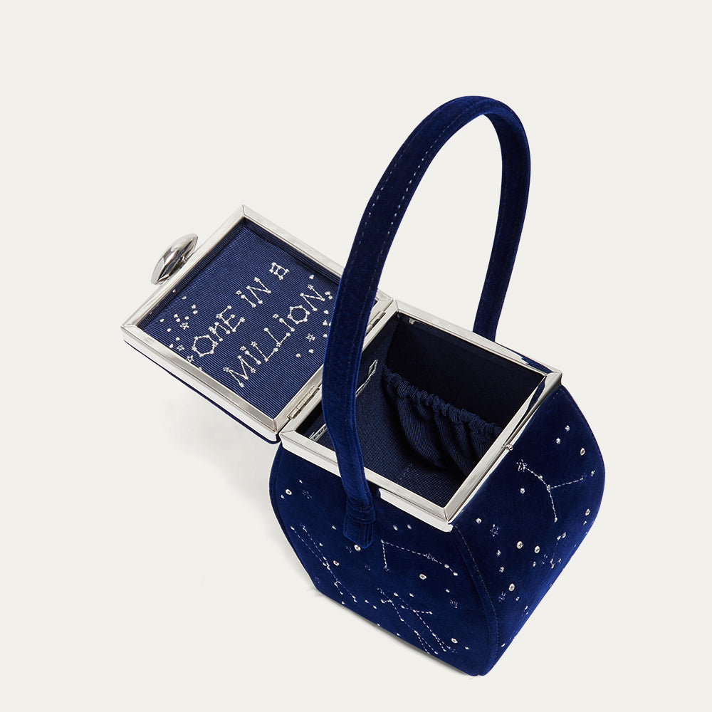 Navy blue velvet handbag with silver clasp and 'One in a Million' text on a white background
