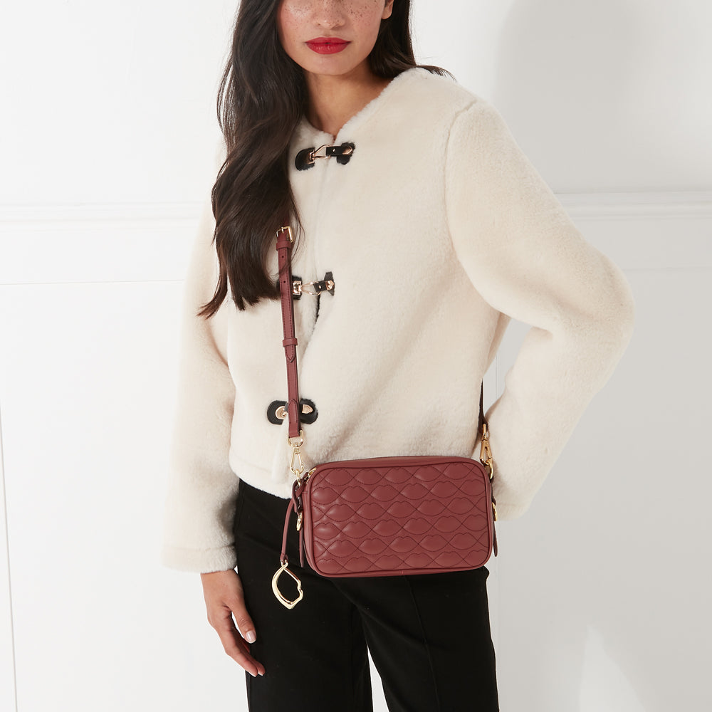 A woman in a cream-colored jacket wears a dark-red quilted crossbody bag with a gold-toned clasp.