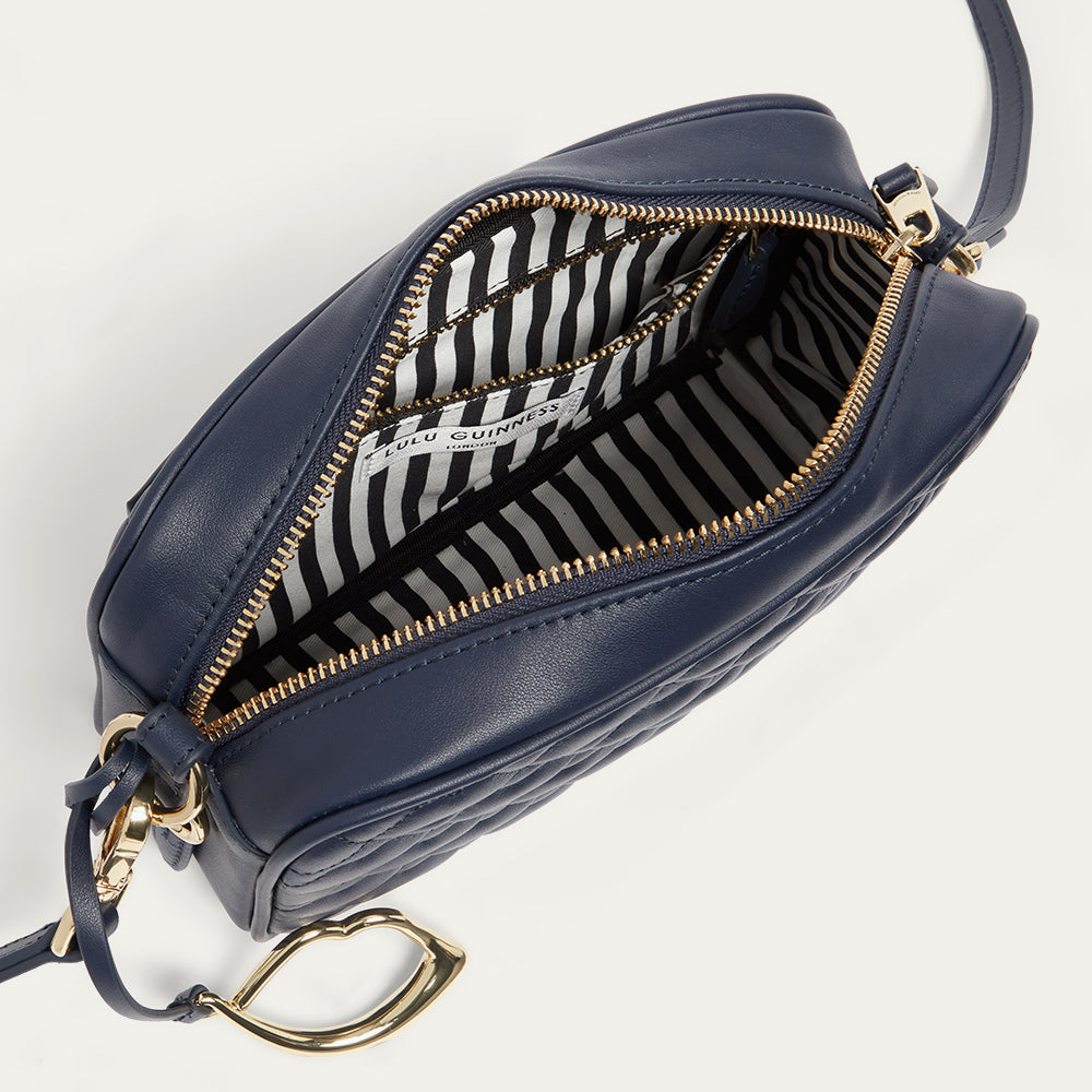 Navy blue leather handbag with gold zipper open revealing a black and white striped lining on a light gray background