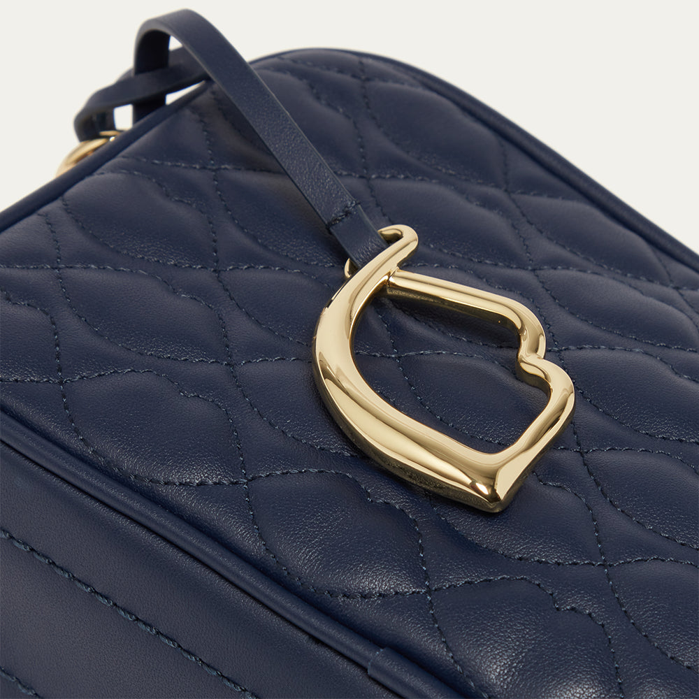 Close-up image of a navy blue leather quilted handbag with a gold lip charm on a light gray background