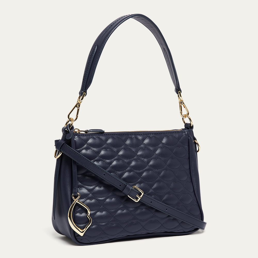 Navy quilted leather handbag with a gold lip charm on a light gray background