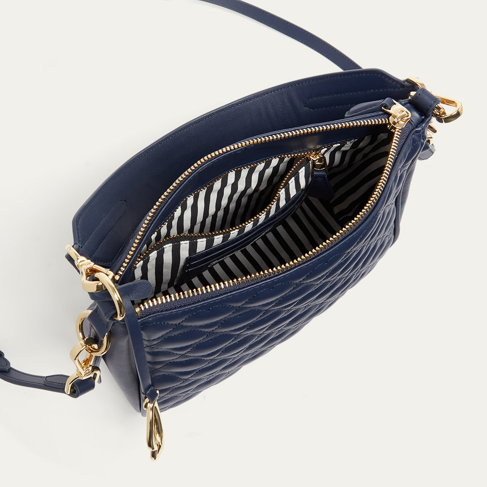 Navy blue leather handbag open revealing a black and white striped lining with gold accents on a white background