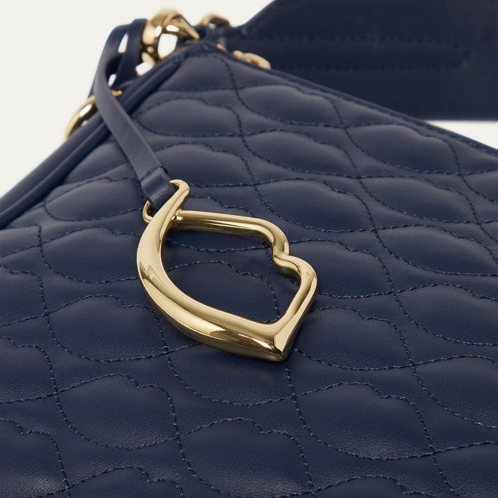 Close-up image of a navy quilted handbag with a gold lip charm on a white background
