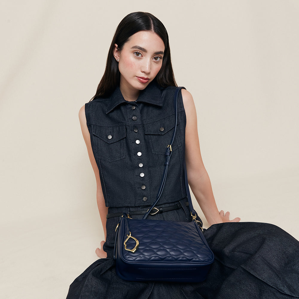 Woman holding a blue quilted handbag with gold lip charm against a beige background