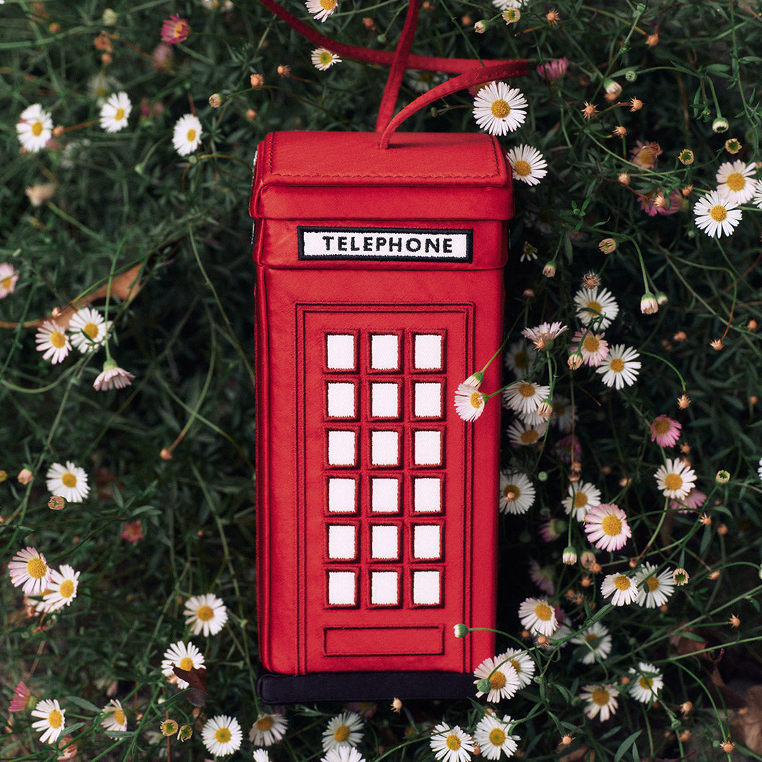 Red phone booth-shaped bag with 'TELEPHONE' label on a floral background