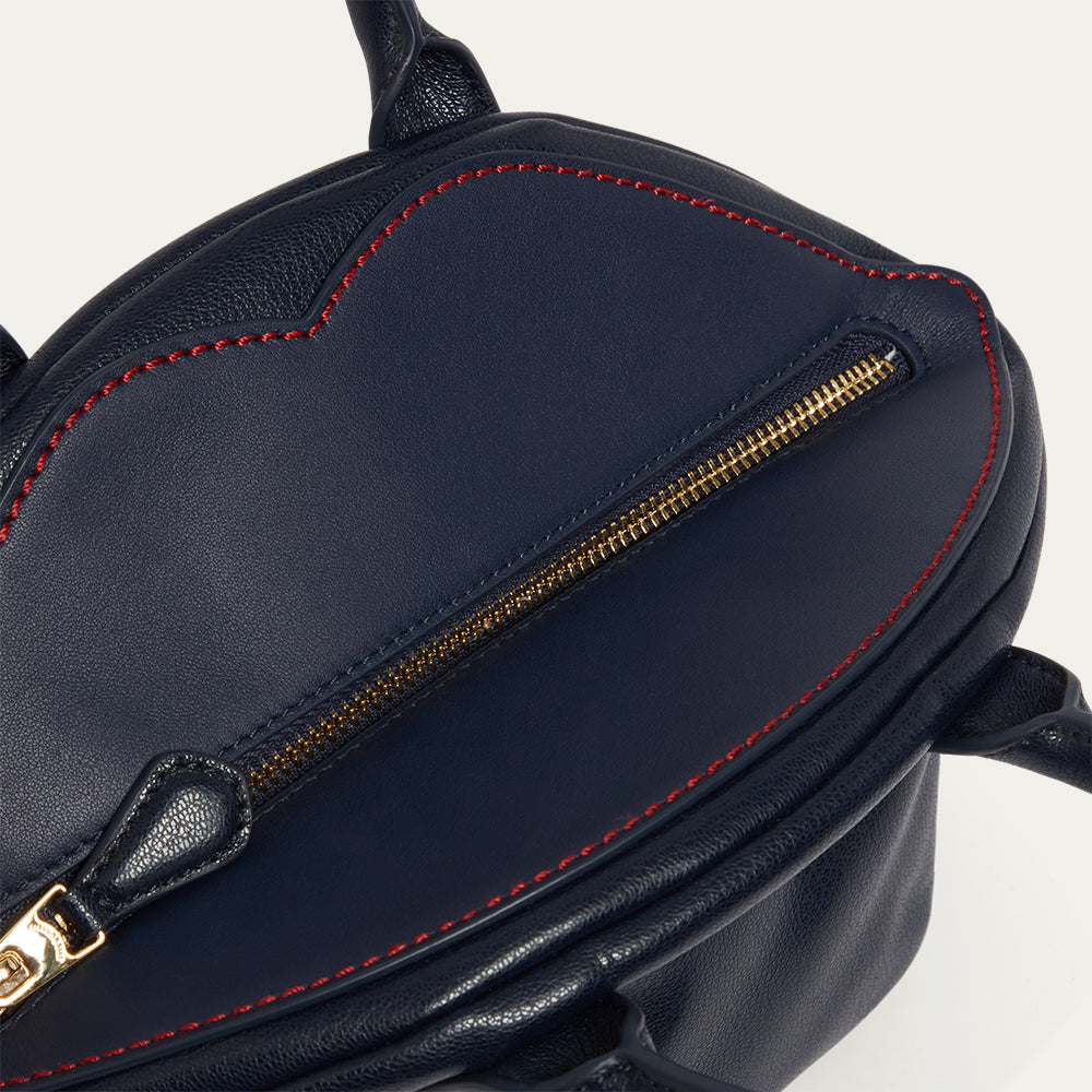 Navy blue leather bag with gold zipper and red stitching on a light gray background