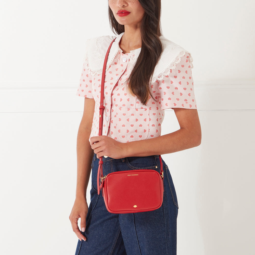 Woman with long brown hair modeling a red crossbody bag against a white background.