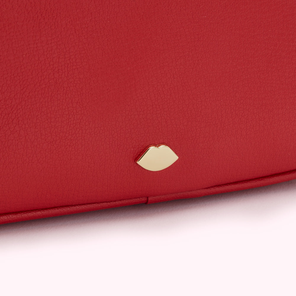 Close-up of a red textured leather purse with a gold lip-shaped logo.
