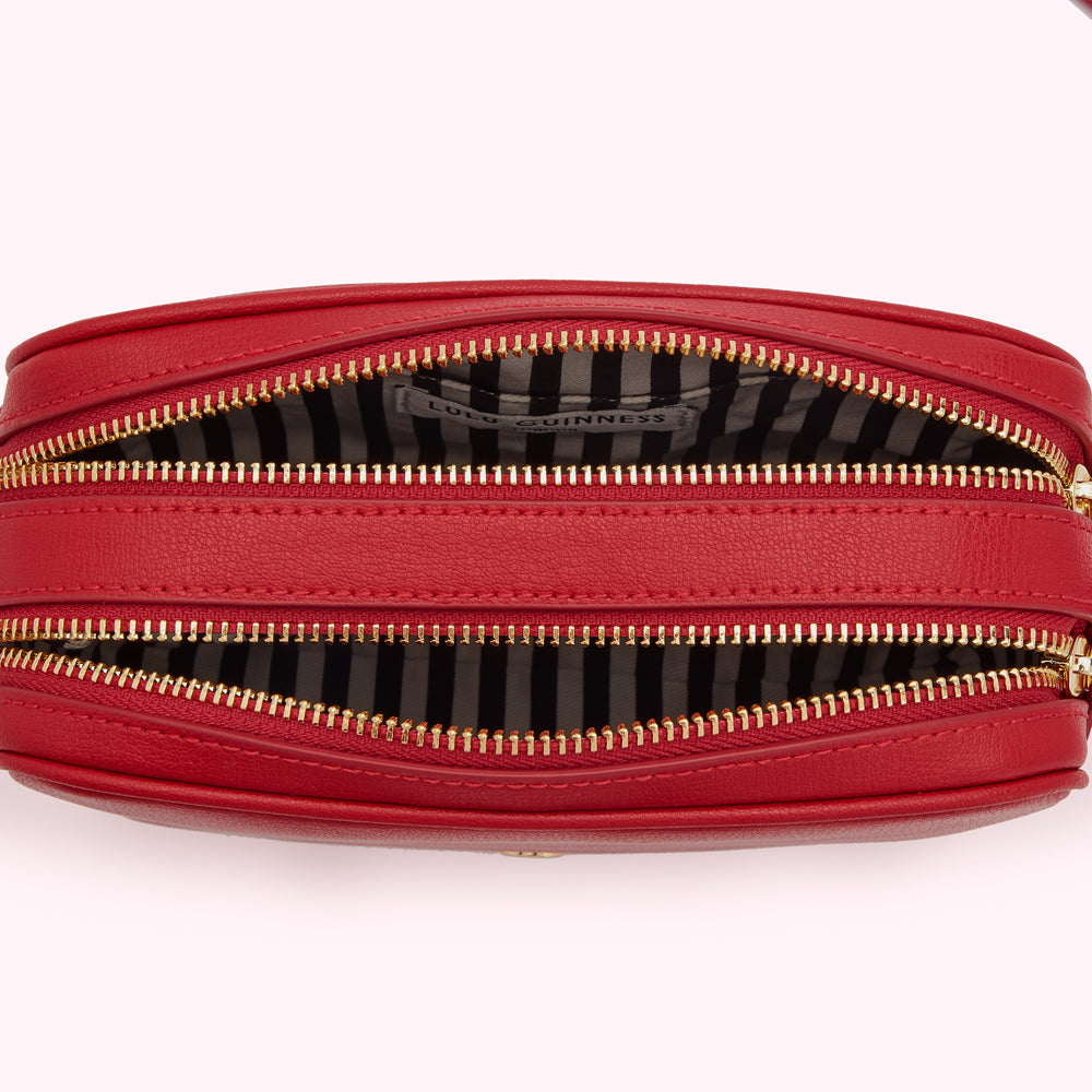 Red Lulu Guinness crossbody bag open to reveal black and white striped interior and gold zippers.
