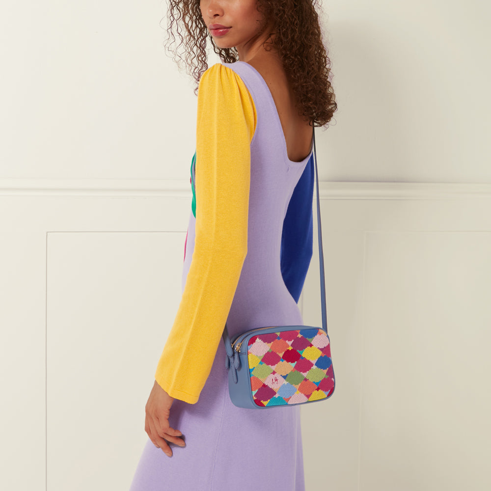 Woman wearing a lavender and yellow dress with a small blue crossbody bag featuring a colorful embroidered pattern.
