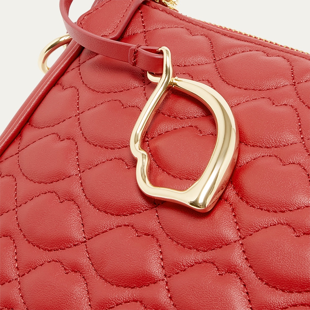Red quilted handbag with a gold lip shaped charm on a light beige background