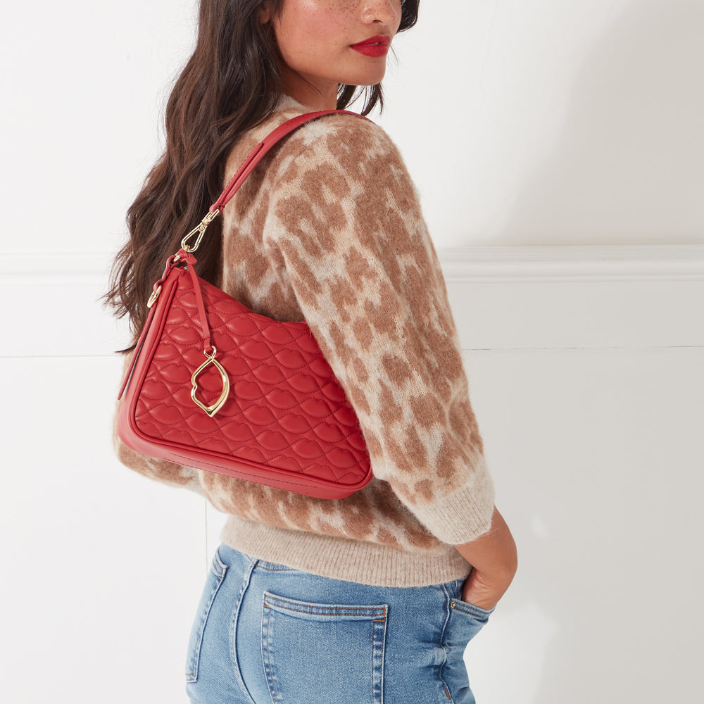 Red quilted shoulder bag with gold lip-shaped charm on a model.