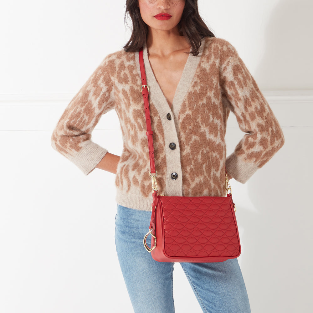 Woman wearing a beige cardigan and blue jeans with a red quilted crossbody bag.