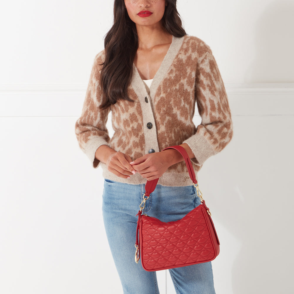 Woman in light brown cardigan holding a red quilted handbag.