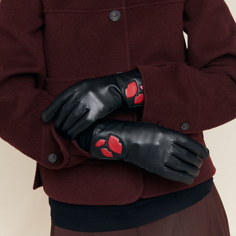 Black gloves with red lip accents worn by a person in a maroon coat.
