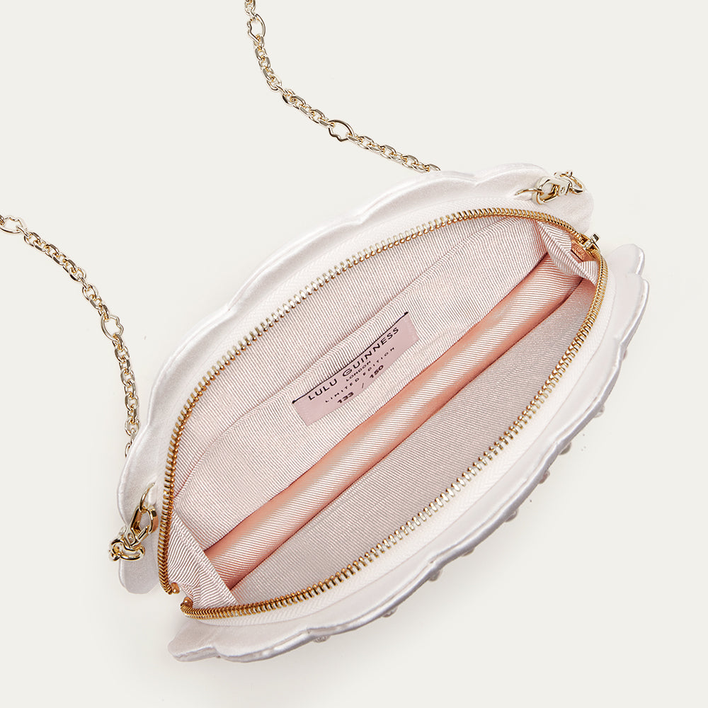White fan shaped handbag open to reveal a blush lining with gold chain strap on a white background
