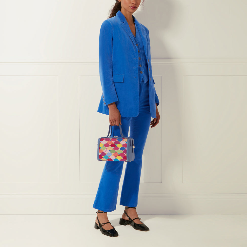 A woman in a bright blue corduroy suit carries a colorful box-shaped handbag.
