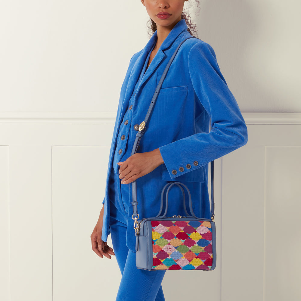 Woman in a blue corduroy suit holding a blue and multicolored patterned handbag.
