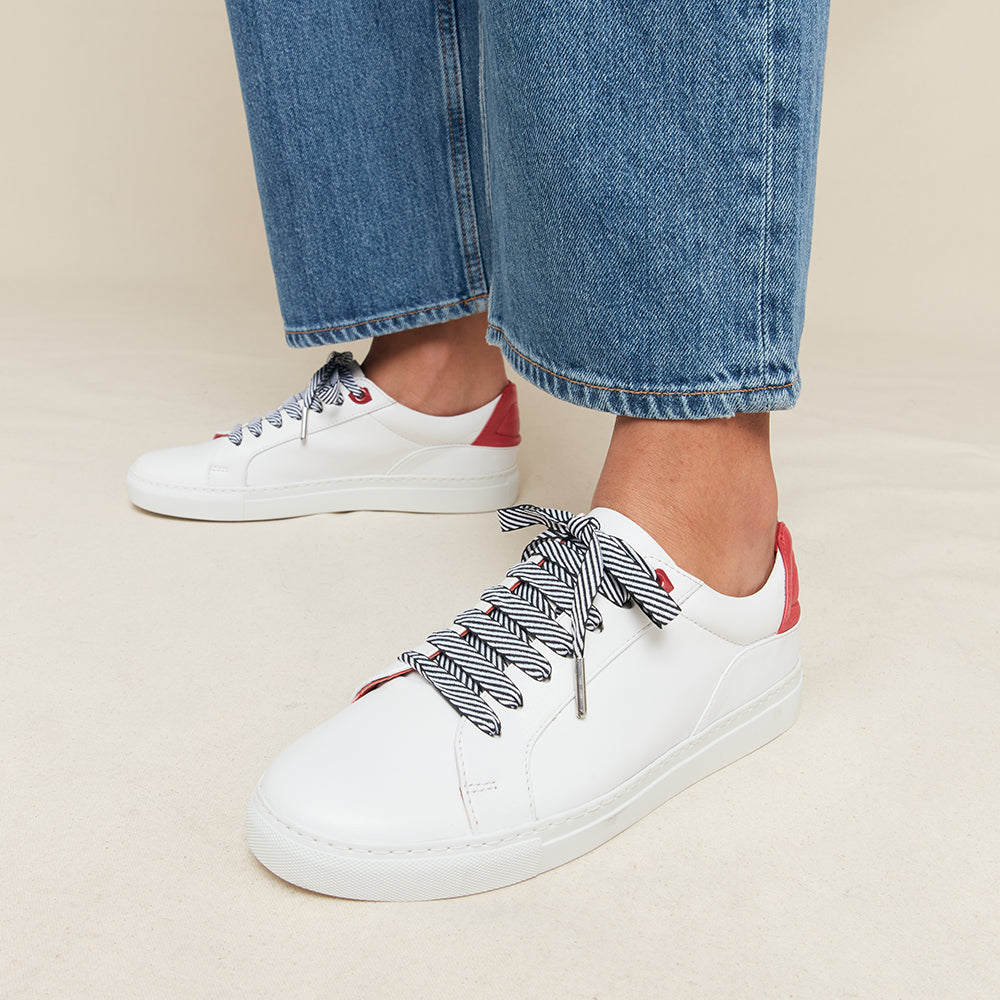 White sneakers with striped laces worn with blue jeans on a beige background