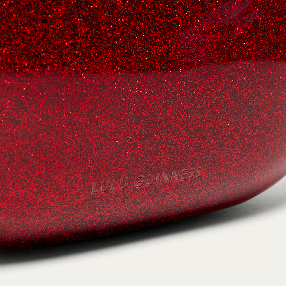 Close-up of a red glittery lip-shaped clutch with 'Lulu Guinness' branding.