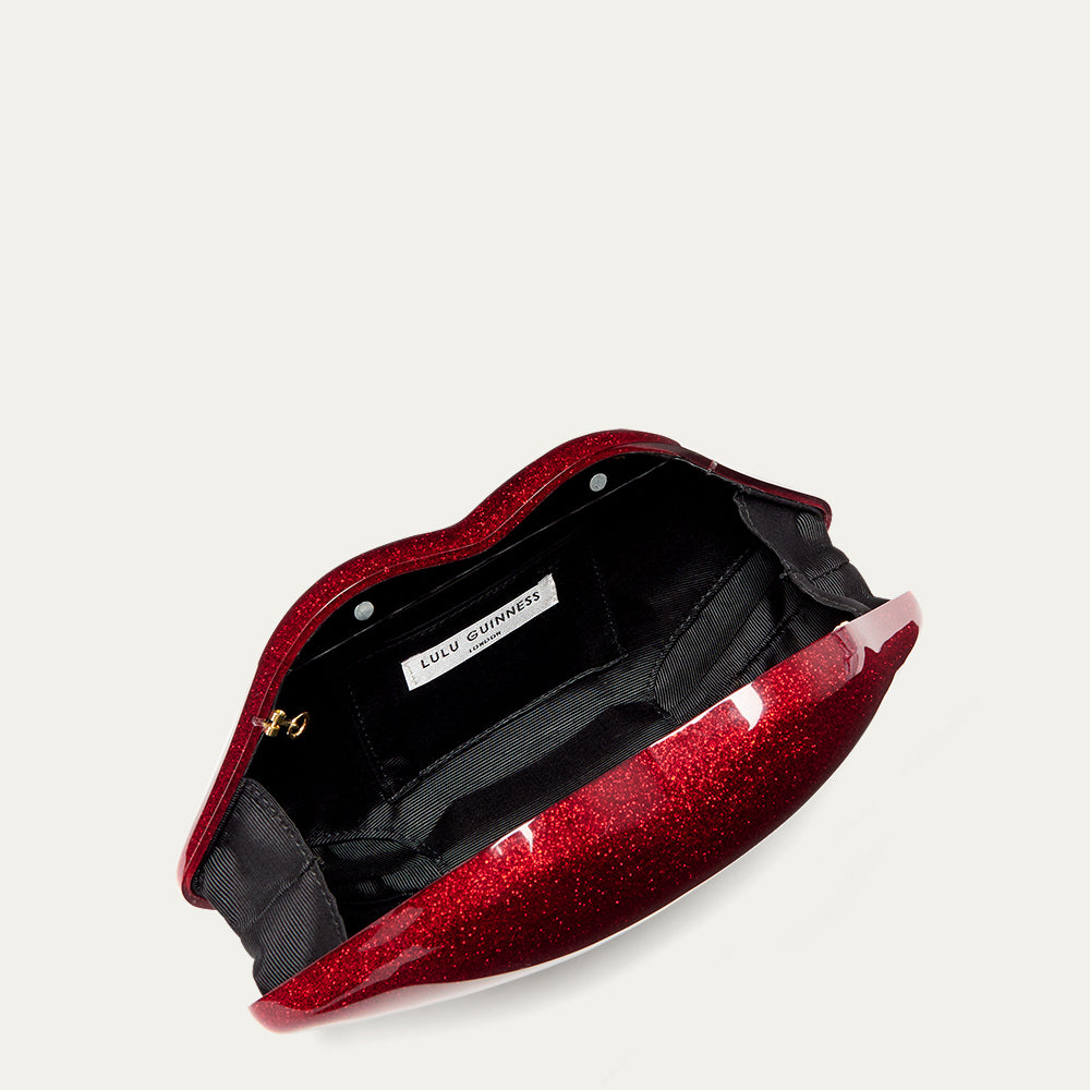 Red glittery clutch bag open revealing a black lining and 'Lulu Guinness' label on a white background