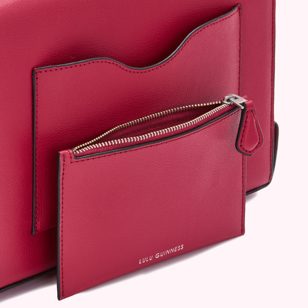 Close-up of a crimson Lulu Guinness handbag's interior, showcasing a zipped pocket and an additional slip pocket.
