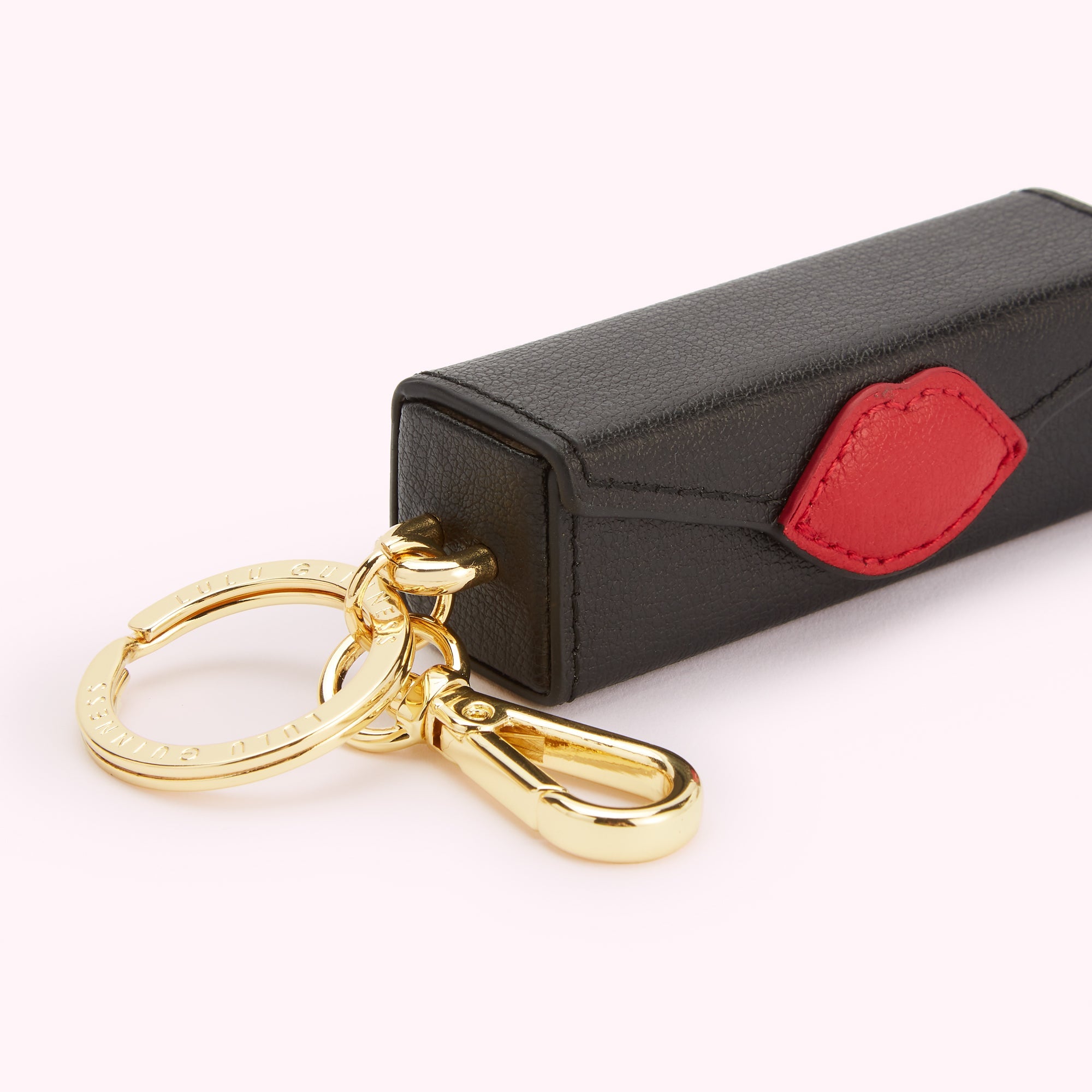 Black leather lipstick-shaped keychain with a red lip detail and gold-tone hardware.
