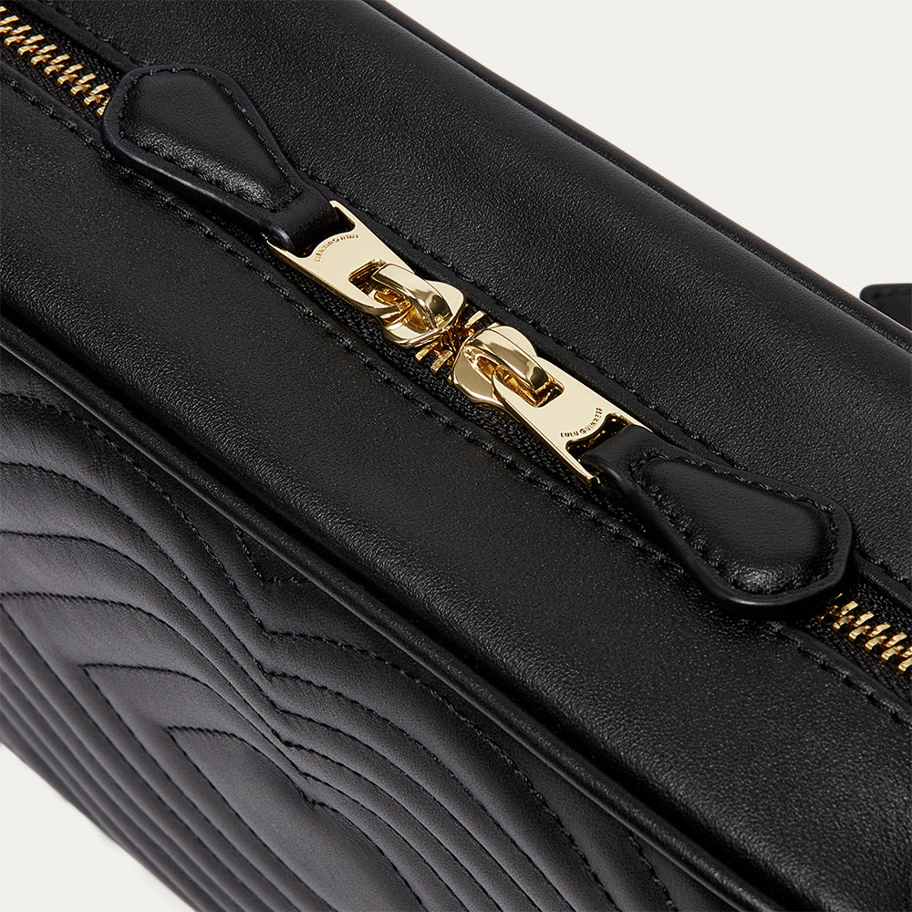 Black handbag with gold zipper on a light gray background