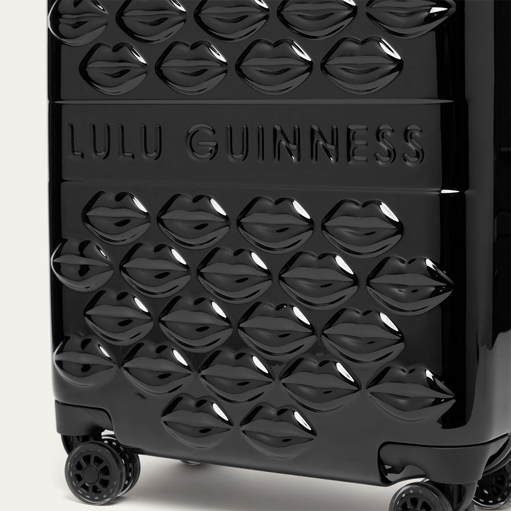 Black suitcase with lips pattern and 'Lulu Guinness' branding on a white background