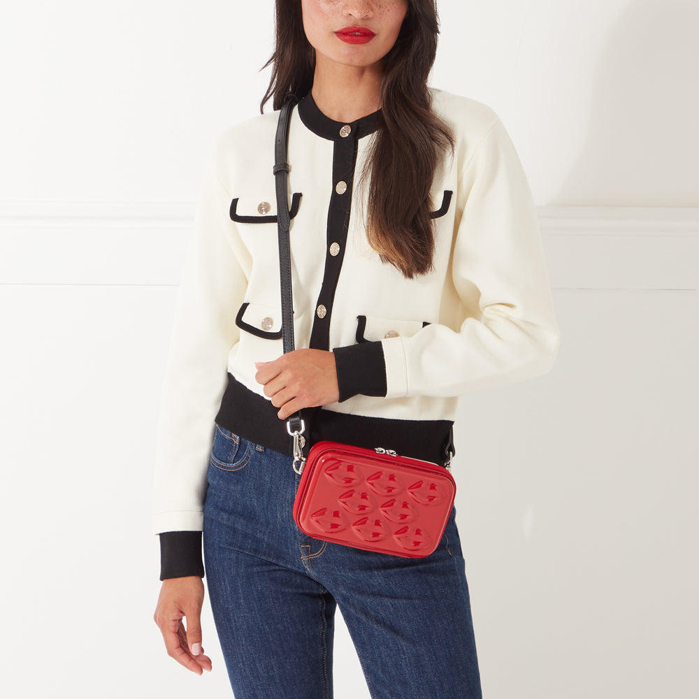 Woman in cream cardigan and jeans holding a red quilted crossbody bag.
