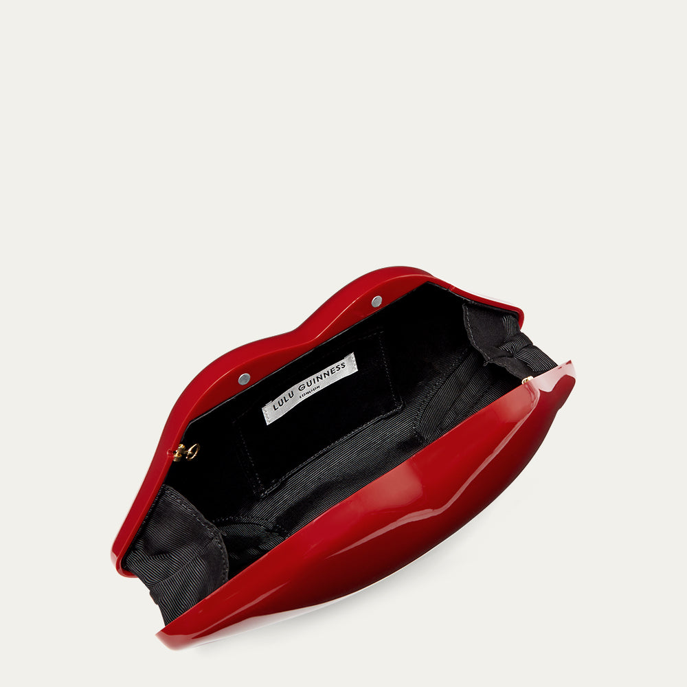 Red lip-shaped clutch bag open to reveal a black lining and a 'Lulu Guinness' branded label on a light gray background