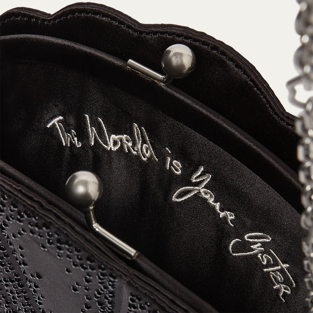 Black handbag with 'The World is Your Oyster' embroidery on a light gray background