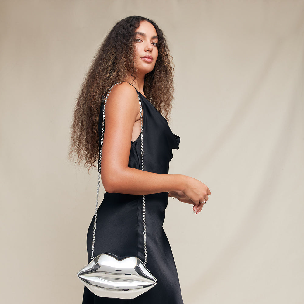 Woman holding a silver lip-shaped handbag against a beige background