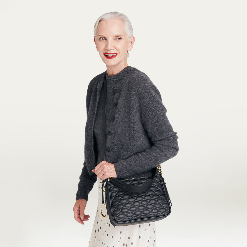 Woman holding a black handbag against a plain background