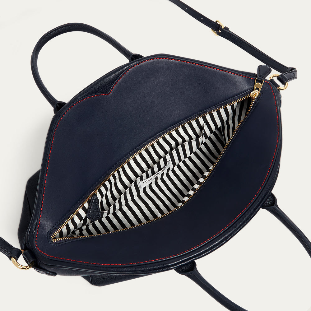 Navy blue leather tote bag with black and white striped lining on a light gray background