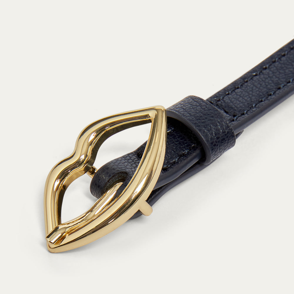 Close up images of a navy leather belt with a gold lip-shaped buckle on a light gray background
